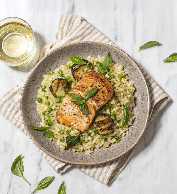 A plate of cooked Arctic Char served on a bed of rice, garnished with green herbs, accompanied by a glass of white wine.