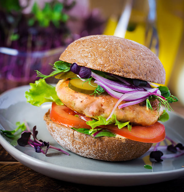 Delicious-looking salmon burger with lettuce, tomato, and onion on a plate.