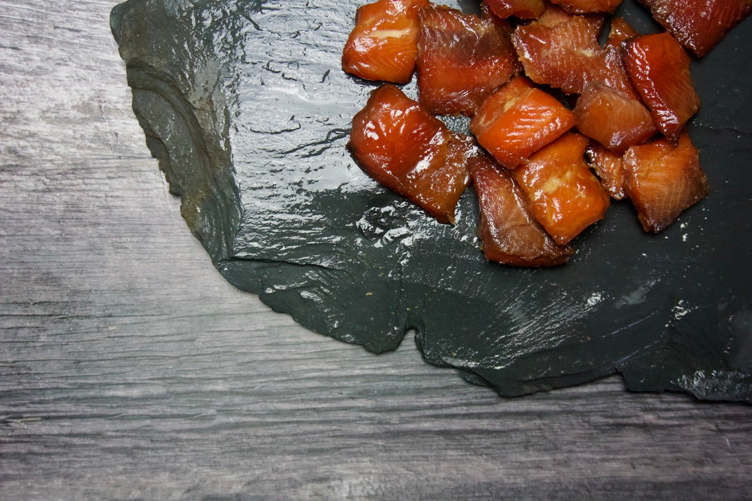 Candied Chinook salmon pieces on a dark slate surface with a wooden background.